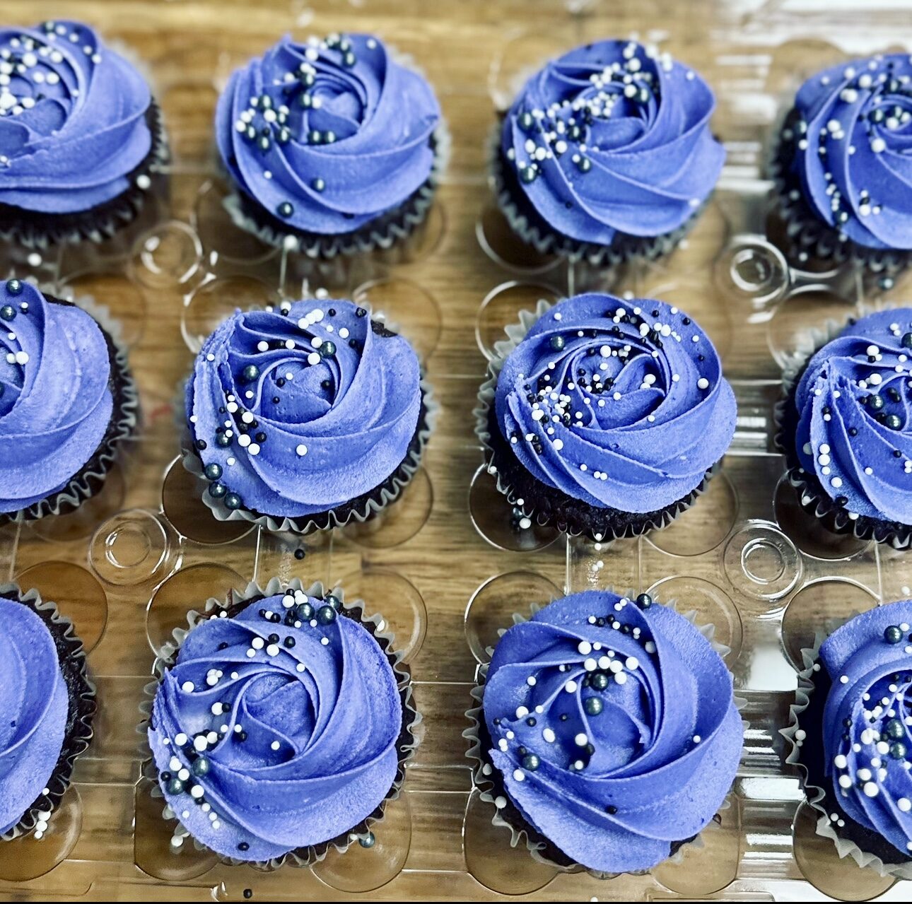 A fresh tray of hand-piped cupcakes beside a small floral cake