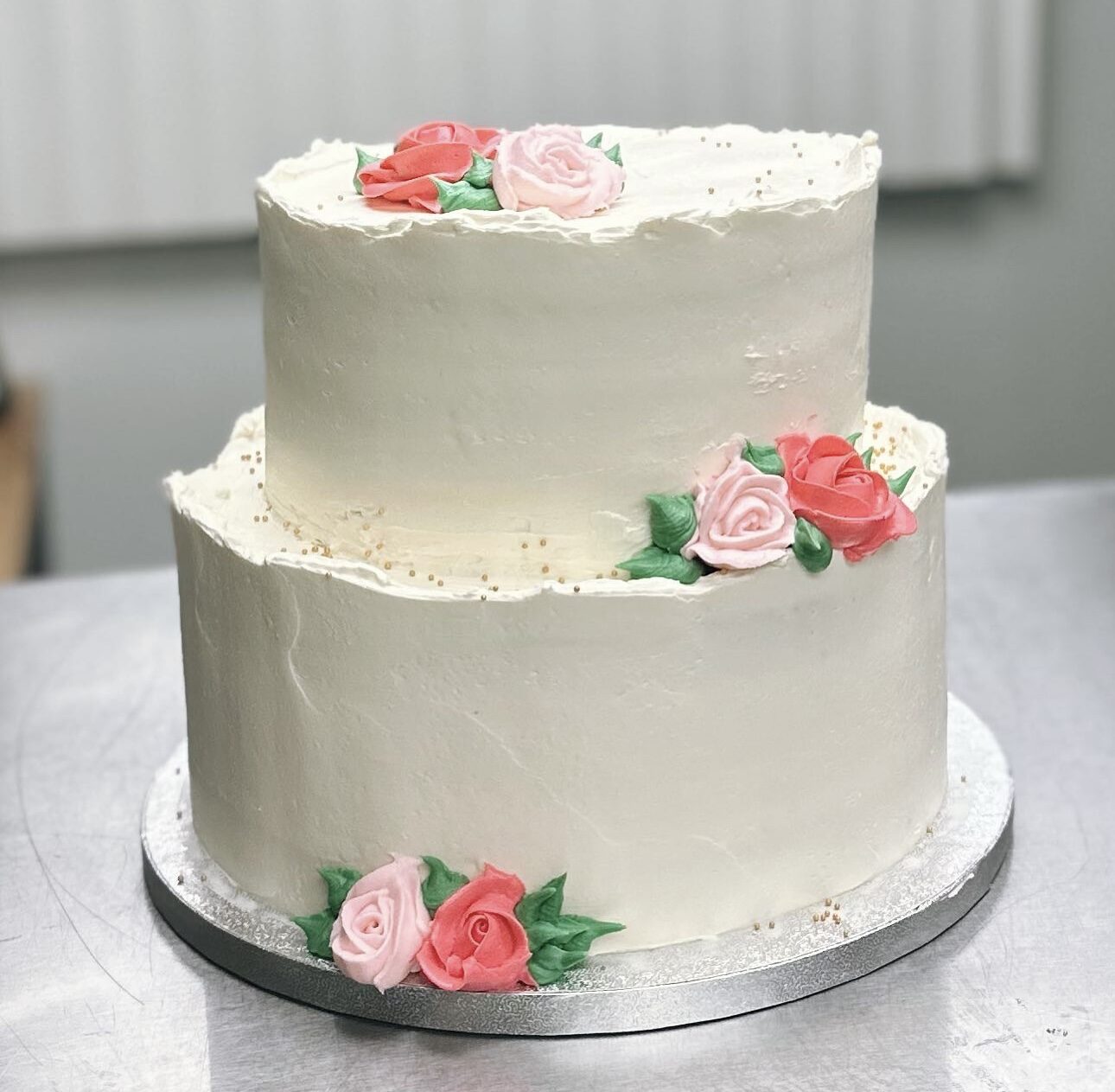 A two-tier buttercream cake decorated with coral and blush sugar roses