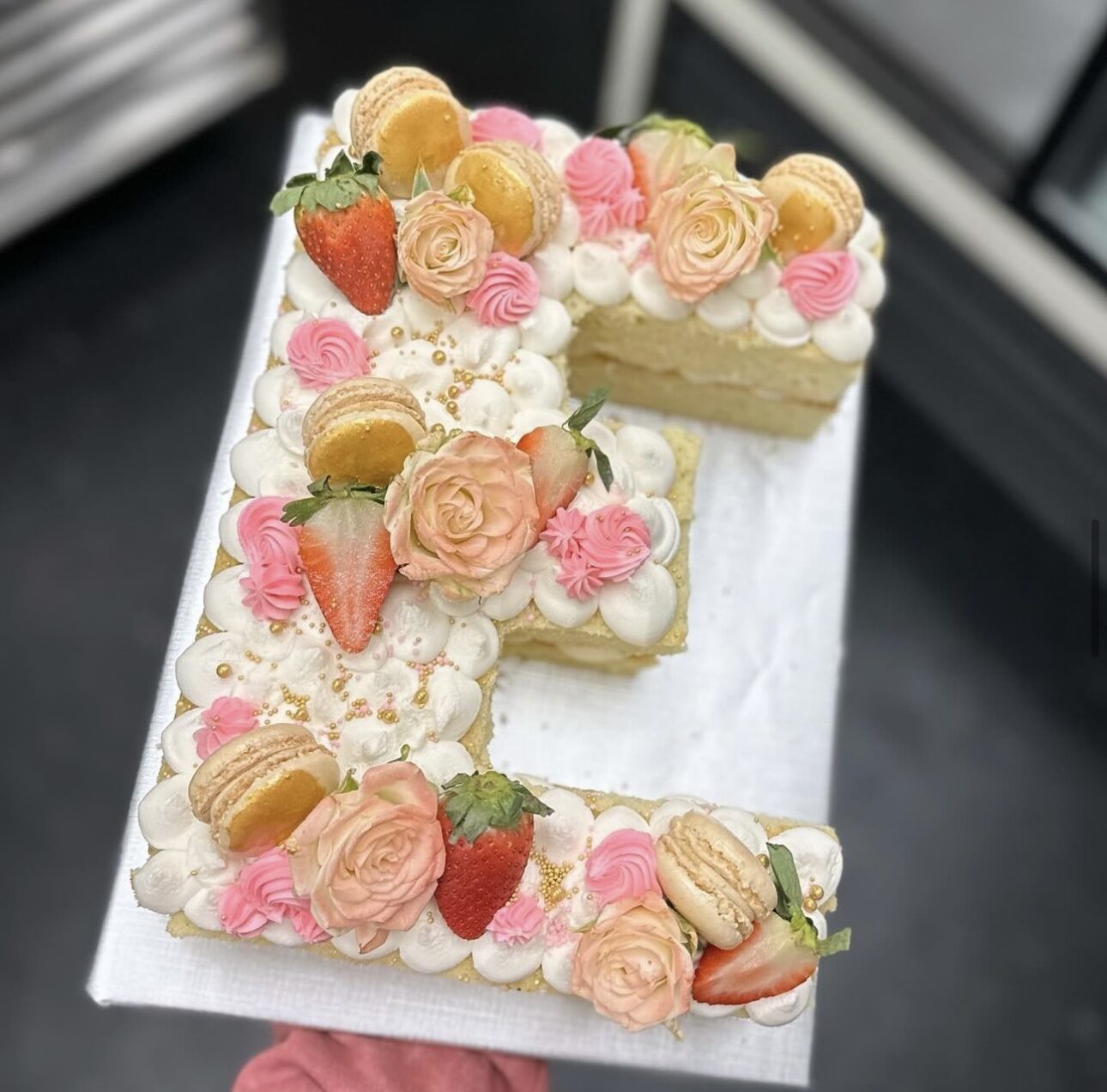 A number cake topped with macarons, berries and buttercream flowers