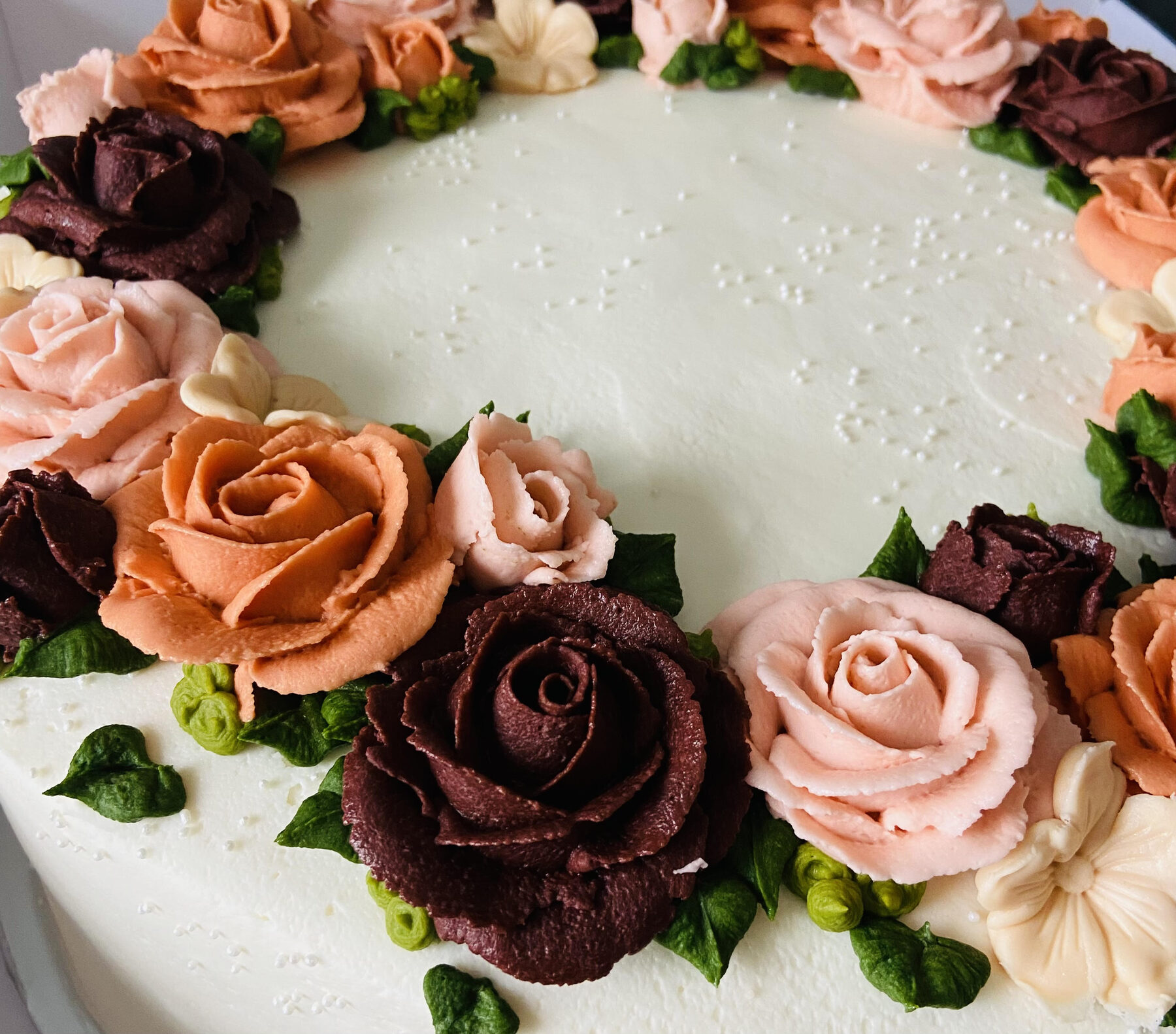 A heart-shaped cake finished with hand-piped buttercream roses in burgundy, mauve and blush